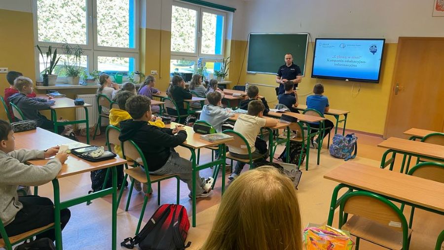 Spotkanie z policjantem, w tle policjant i uczniowie